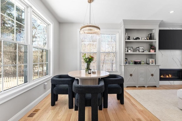 dining space featuring a chandelier, a fireplace, visible vents, baseboards, and light wood-style floors