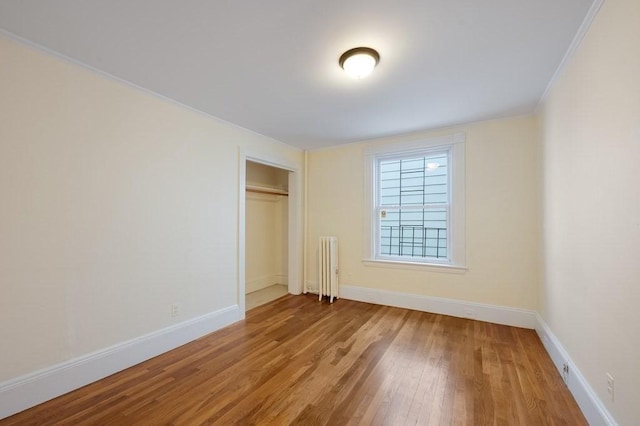 unfurnished bedroom with radiator heating unit, wood finished floors, baseboards, a closet, and crown molding
