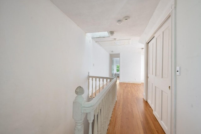 hallway featuring light wood-style flooring, an upstairs landing, and attic access