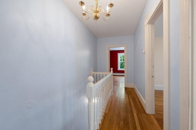 corridor featuring an upstairs landing, a chandelier, wood finished floors, and baseboards