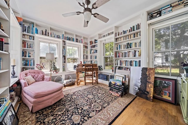 living area featuring ceiling fan, wood-type flooring, bookshelves, and built in shelves
