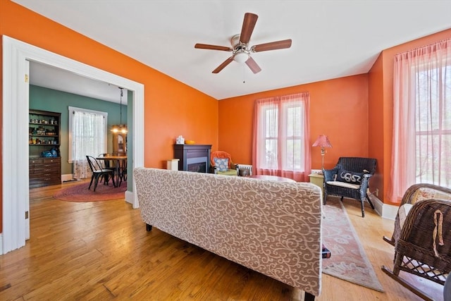 living room with baseboards, wood finished floors, and ceiling fan with notable chandelier