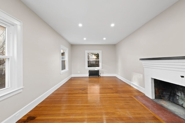 unfurnished living room featuring radiator heating unit, light hardwood / wood-style flooring, and a brick fireplace