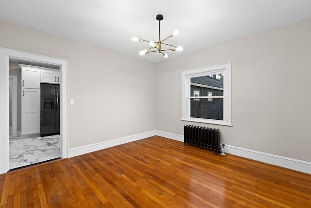 spare room featuring hardwood / wood-style flooring, radiator heating unit, and an inviting chandelier