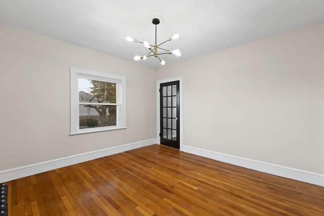 empty room featuring wood-type flooring and an inviting chandelier