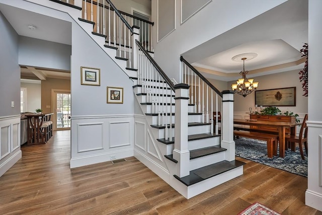 stairs with crown molding, wood-type flooring, and a notable chandelier