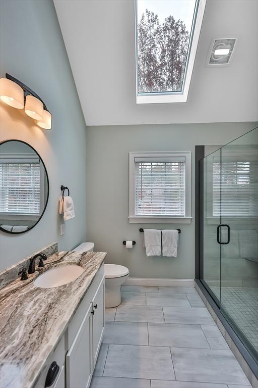 bathroom with vaulted ceiling with skylight, toilet, a shower with door, and vanity