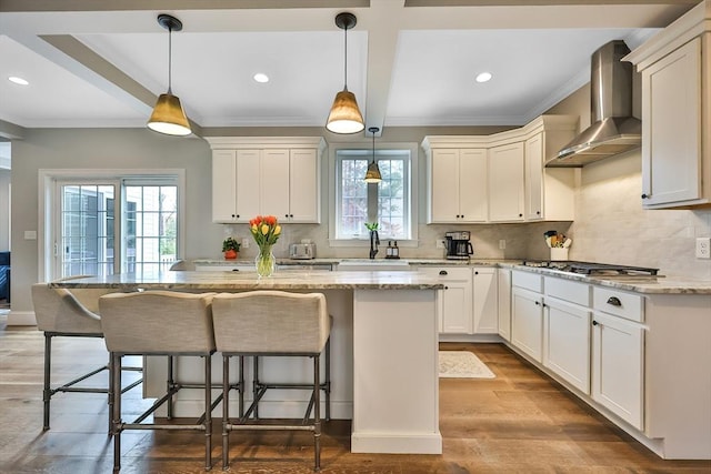 kitchen featuring stainless steel gas stovetop, wall chimney range hood, light stone counters, and pendant lighting