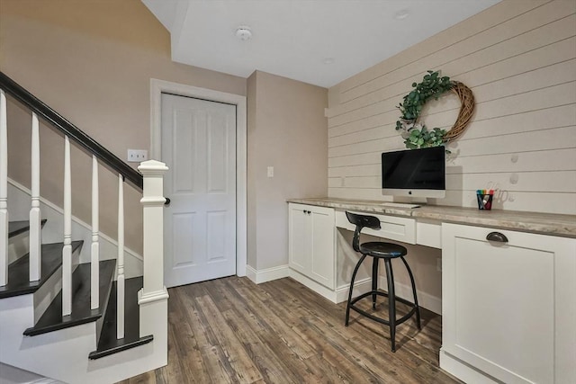 office featuring built in desk, dark hardwood / wood-style floors, and wood walls