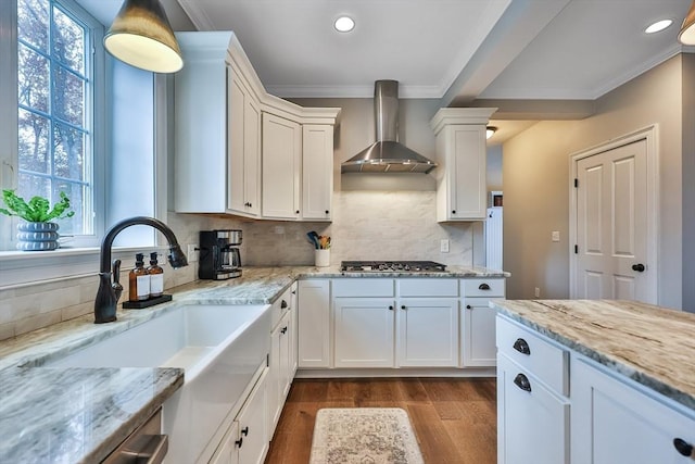 kitchen with tasteful backsplash, stainless steel gas stovetop, wall chimney range hood, light stone countertops, and white cabinets