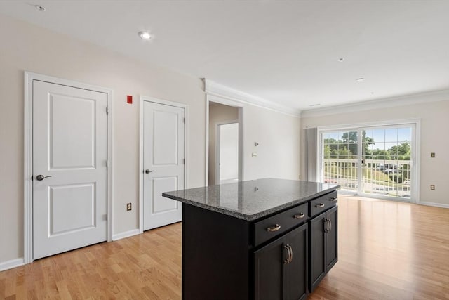 kitchen with a center island, light hardwood / wood-style floors, ornamental molding, and dark stone countertops