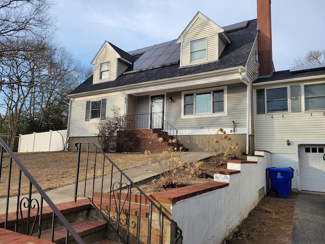 cape cod-style house with roof mounted solar panels, roof with shingles, fence, and a chimney