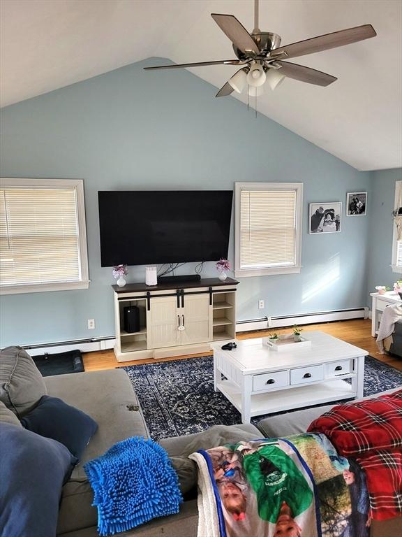 living area with light wood-style floors, lofted ceiling, and baseboard heating