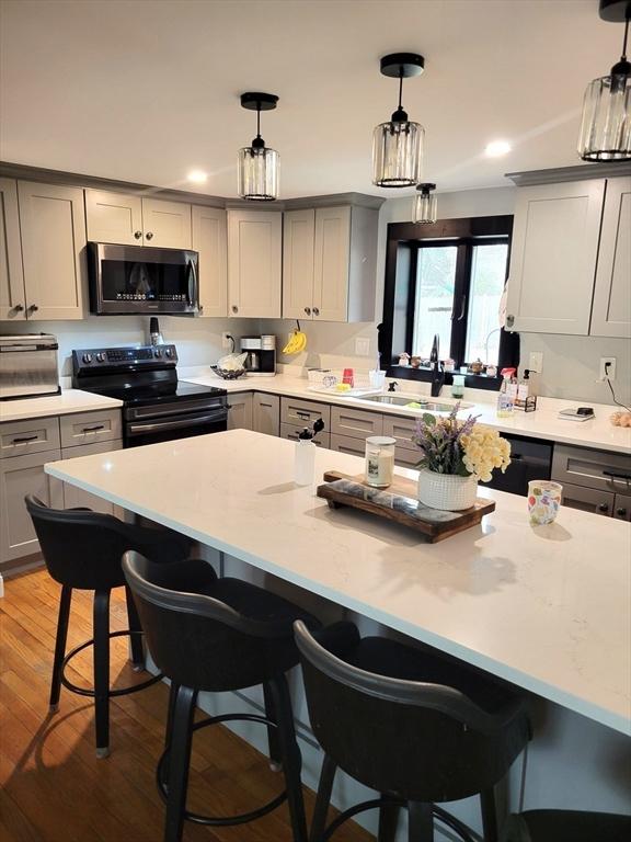 kitchen featuring range with electric cooktop, stainless steel microwave, gray cabinets, a kitchen bar, and a sink