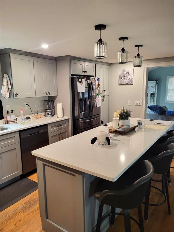 kitchen featuring a breakfast bar area, gray cabinetry, light countertops, and black appliances