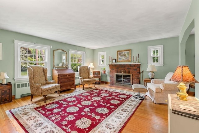 52 Harding Rd, Lexington, MA 02420 - living room featuring radiator heating unit, light wood-type flooring, a brick fireplace, and a textured ceiling
