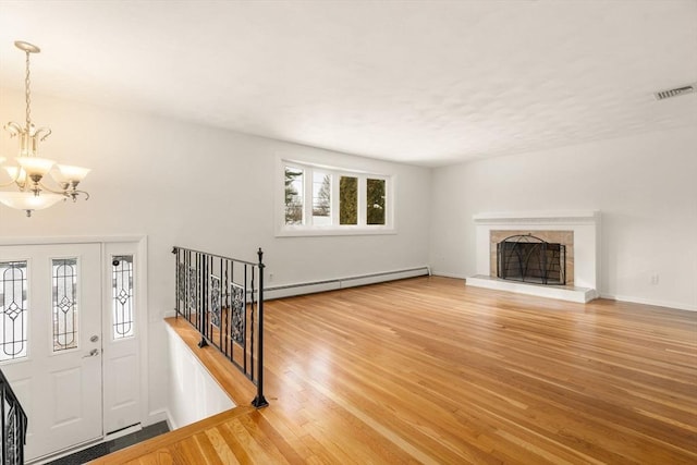 unfurnished living room with baseboard heating, a chandelier, hardwood / wood-style floors, and a tile fireplace