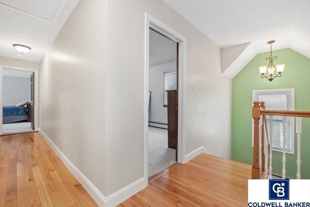 hallway with a baseboard heating unit, vaulted ceiling, an upstairs landing, wood finished floors, and baseboards