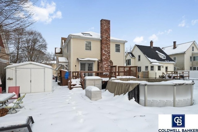 snow covered property with a storage shed, a chimney, an outbuilding, and a wooden deck