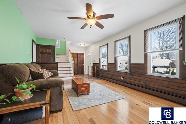 living area with a wainscoted wall, a baseboard heating unit, wooden walls, hardwood / wood-style floors, and stairs