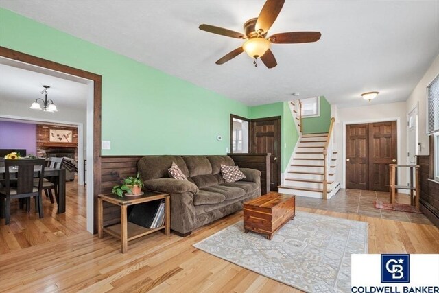 living area featuring ceiling fan with notable chandelier, a fireplace, stairway, and wood finished floors