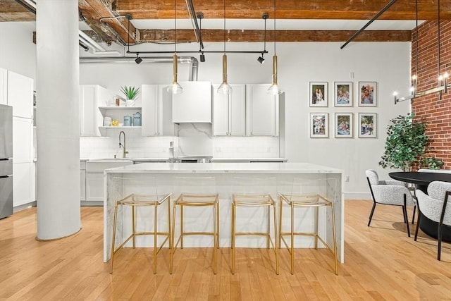 33 Sleeper St Unit 106, Boston, MA 02210 - kitchen featuring open shelves, light wood finished floors, white cabinetry, tasteful backsplash, and a high ceiling