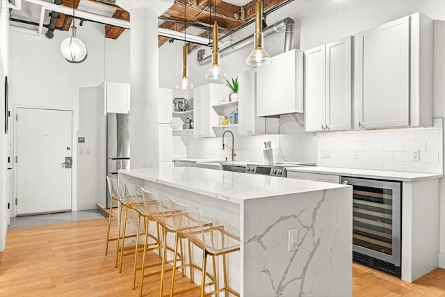 33 Sleeper St Unit 106, Boston, MA 02210 - kitchen featuring beverage cooler, open shelves, appliances with stainless steel finishes, a center island, and backsplash