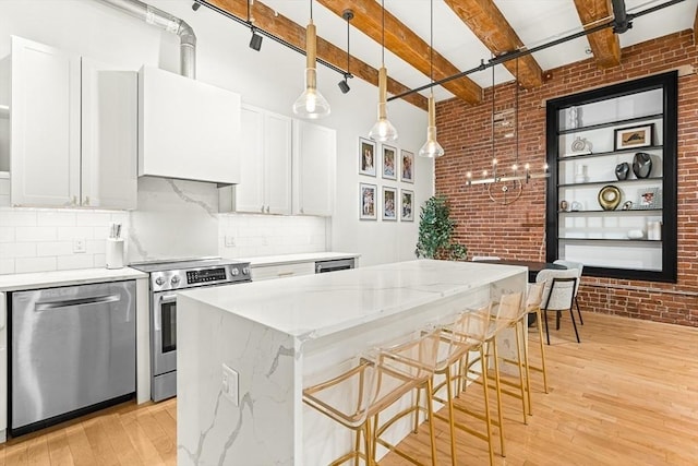 33 Sleeper St Unit 106, Boston, MA 02210 - kitchen with stainless steel appliances, brick wall, light wood-style flooring, decorative backsplash, and a center island