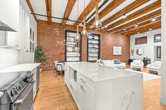 33 Sleeper St Unit 106, Boston, MA 02210 - kitchen with stainless steel range with electric stovetop, brick wall, white cabinetry, light wood-style floors, and beam ceiling