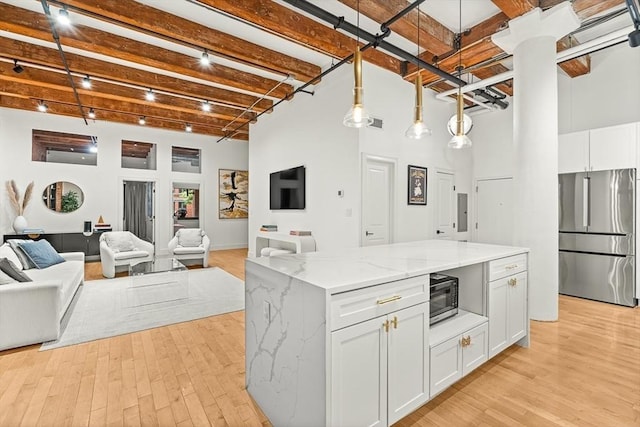 33 Sleeper St Unit 106, Boston, MA 02210 - kitchen featuring stainless steel appliances, beamed ceiling, white cabinets, light wood-style floors, and light stone countertops