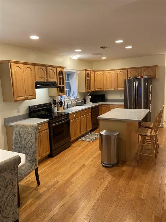 52 Cranberry Rd, Hanson, MA 02341 - kitchen with black appliances, under cabinet range hood, glass insert cabinets, a kitchen bar, and light wood-style floors