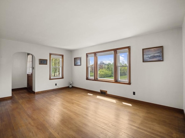 unfurnished room with arched walkways, hardwood / wood-style flooring, and baseboards