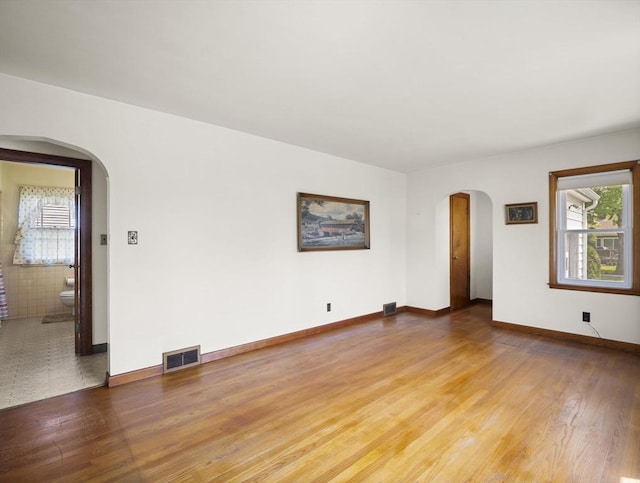 spare room featuring arched walkways, wood finished floors, and baseboards