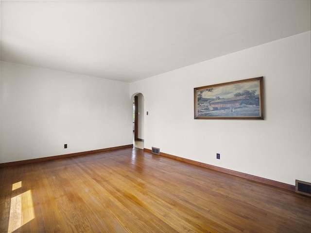 unfurnished room featuring arched walkways, light wood-type flooring, and baseboards
