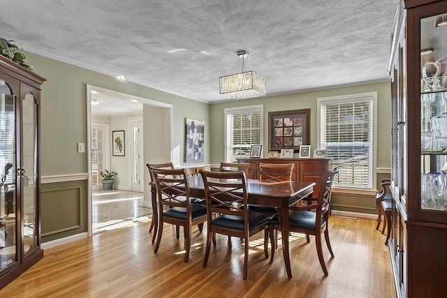 dining room with ornamental molding, light hardwood / wood-style floors, and a textured ceiling