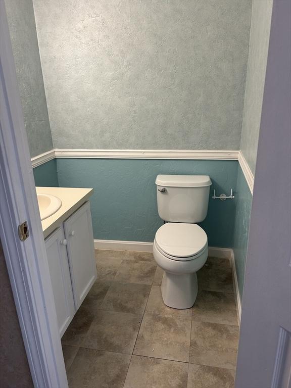 half bathroom featuring toilet, tile patterned floors, baseboards, and vanity