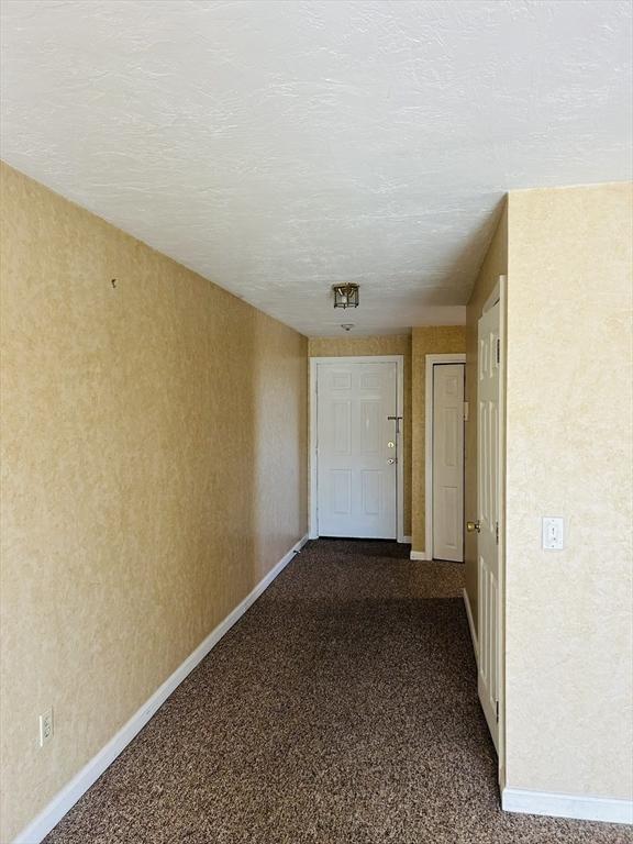 hall with baseboards and dark colored carpet