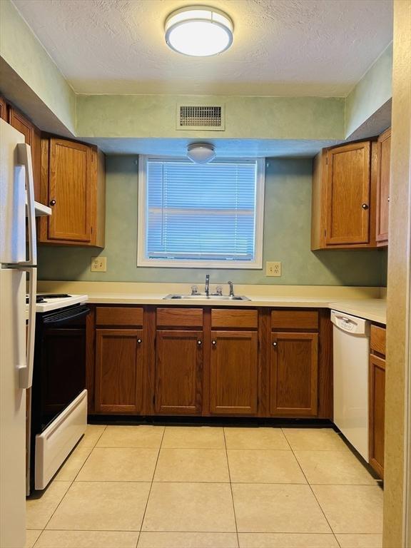 kitchen featuring light tile patterned floors, white appliances, a sink, visible vents, and light countertops