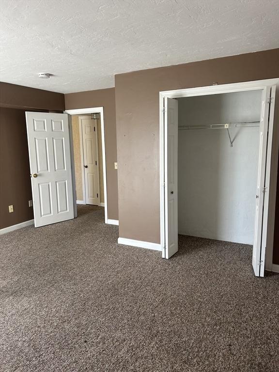 unfurnished bedroom featuring a textured ceiling, a closet, baseboards, and carpet flooring