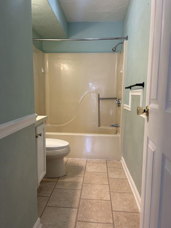 full bathroom with a textured ceiling, tile patterned flooring, toilet, vanity, and washtub / shower combination