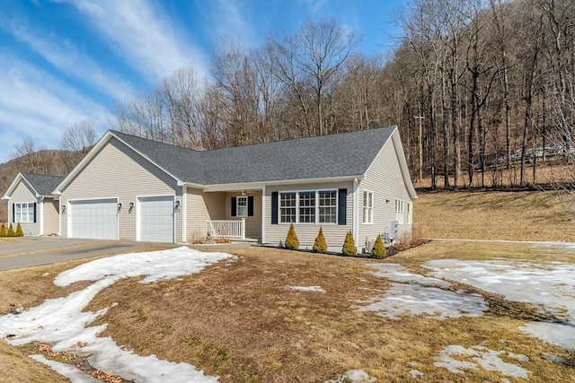 ranch-style house featuring aphalt driveway, an attached garage, covered porch, and a shingled roof