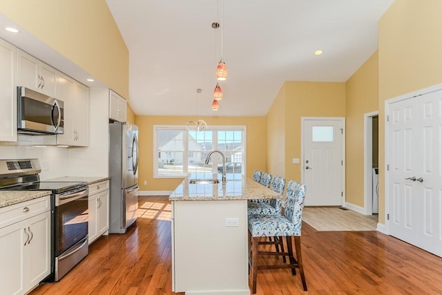 kitchen featuring an island with sink, lofted ceiling, wood finished floors, stainless steel appliances, and a sink