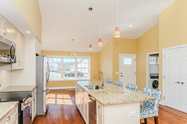 kitchen featuring wood finished floors, washer / clothes dryer, stainless steel appliances, a sink, and a kitchen bar