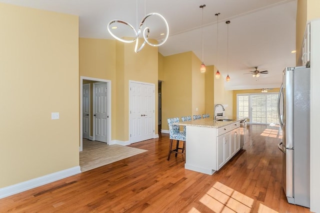 kitchen featuring light wood finished floors, a breakfast bar, freestanding refrigerator, white cabinets, and a sink