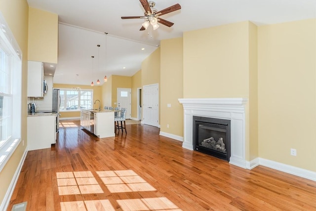 unfurnished living room with light wood-type flooring, visible vents, a ceiling fan, a glass covered fireplace, and baseboards