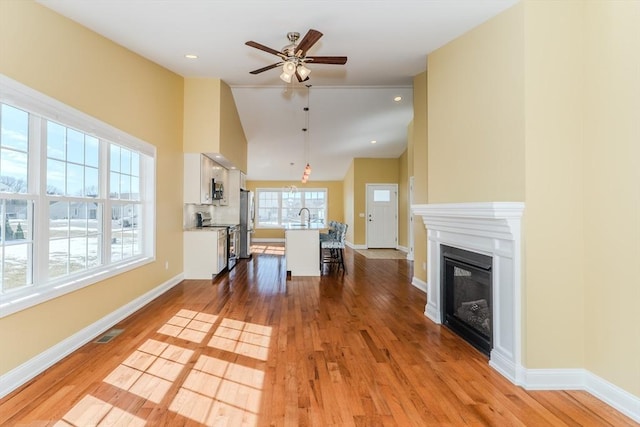 unfurnished living room featuring visible vents, baseboards, a glass covered fireplace, and wood finished floors