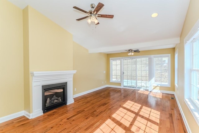 unfurnished living room featuring ceiling fan, baseboards, vaulted ceiling, light wood-style floors, and a glass covered fireplace