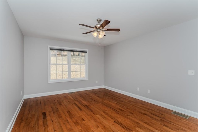 spare room with ceiling fan, visible vents, baseboards, and wood finished floors