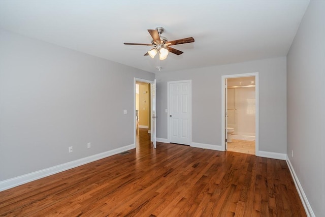 unfurnished bedroom with visible vents, a ceiling fan, ensuite bath, wood finished floors, and baseboards