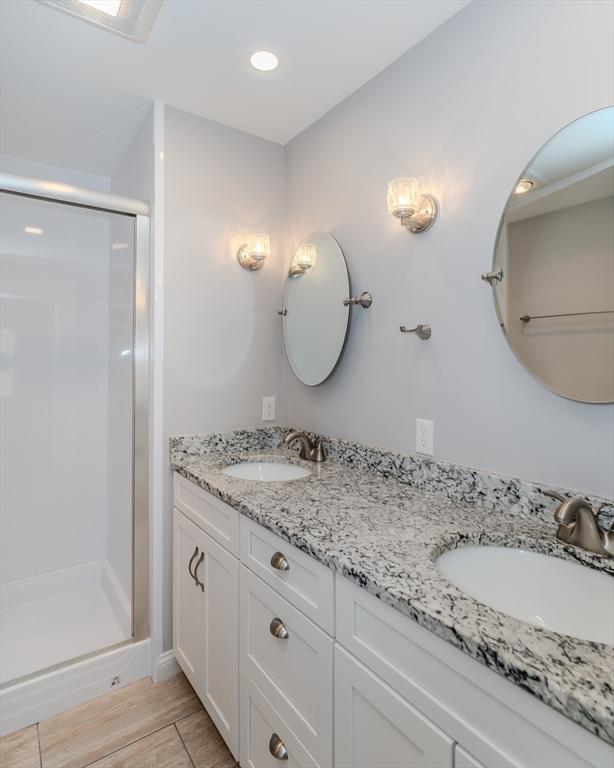 bathroom featuring double vanity, a shower stall, wood finish floors, and a sink